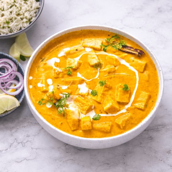 Creamy orange paneer curry with cilantro, a side of rice, red onions, and lime wedges.