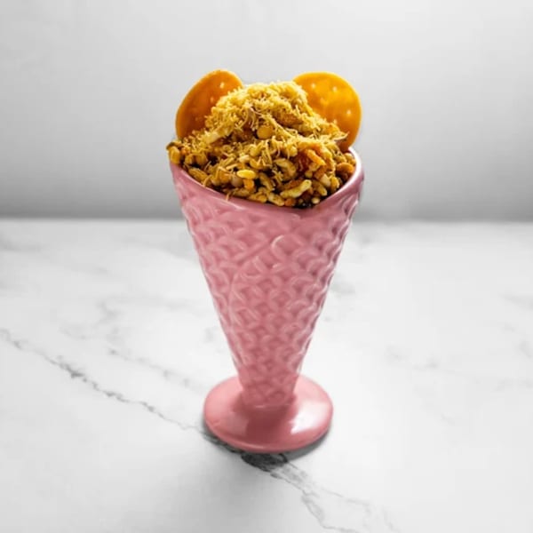 Indian snack mix, bhel puri, served in a pink textured cone with two round crackers.