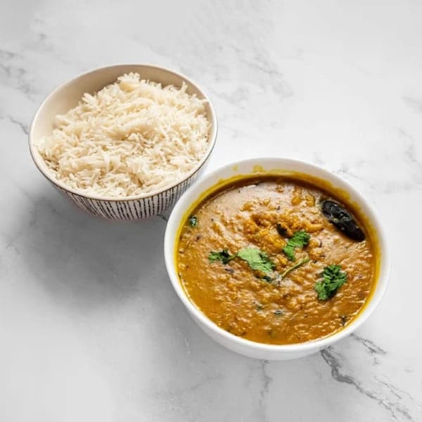 A bowl of Masala Symphony's Indian dal with cilantro, next to a bowl of white rice.