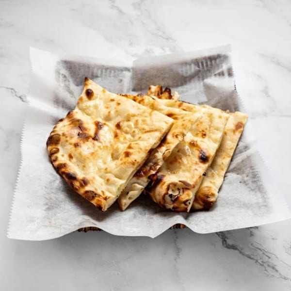 Golden brown naan bread, cut into triangles, served in a basket lined with white paper.