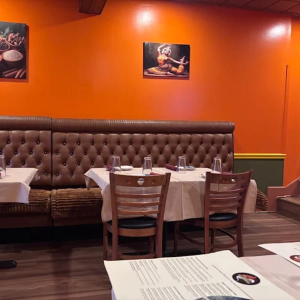 Interior of Masala Symphony with orange walls, brown booths, and set tables with white tablecloths.