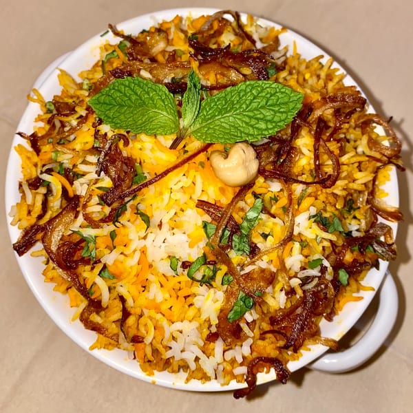 Masala Symphony's Indian biryani, garnished with mint, fried onions, and a cashew, in a white bowl.