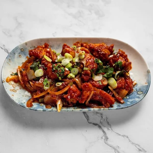 Masala Symphony's chili chicken, a vibrant Indian dish with red sauce, onions, and green garnishes.