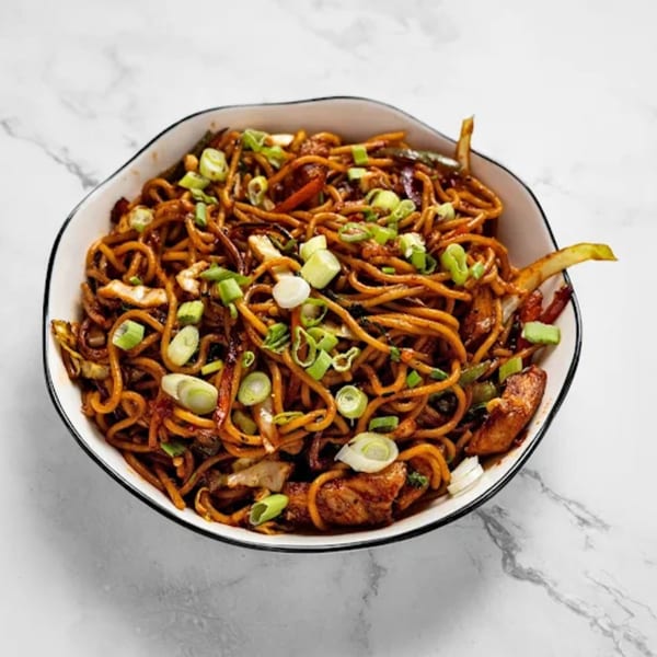 A bowl of Masala Symphony's Indian noodles with chicken and green onions on a marble surface.