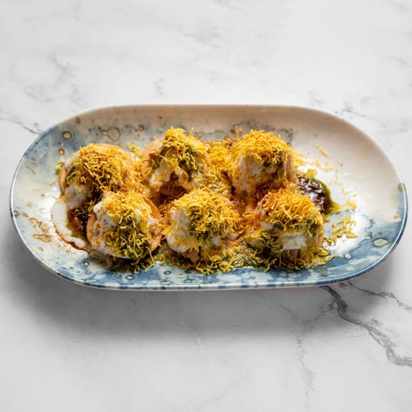 Masala Symphony's Indian chaat, crispy fried dough topped with yogurt, chutneys, and sev on a blue plate.
