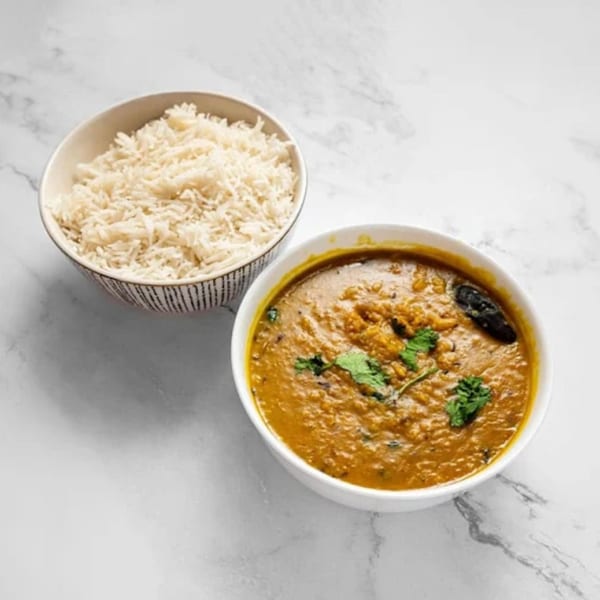 A bowl of Masala Symphony's Indian dal with cilantro, next to a bowl of white rice.